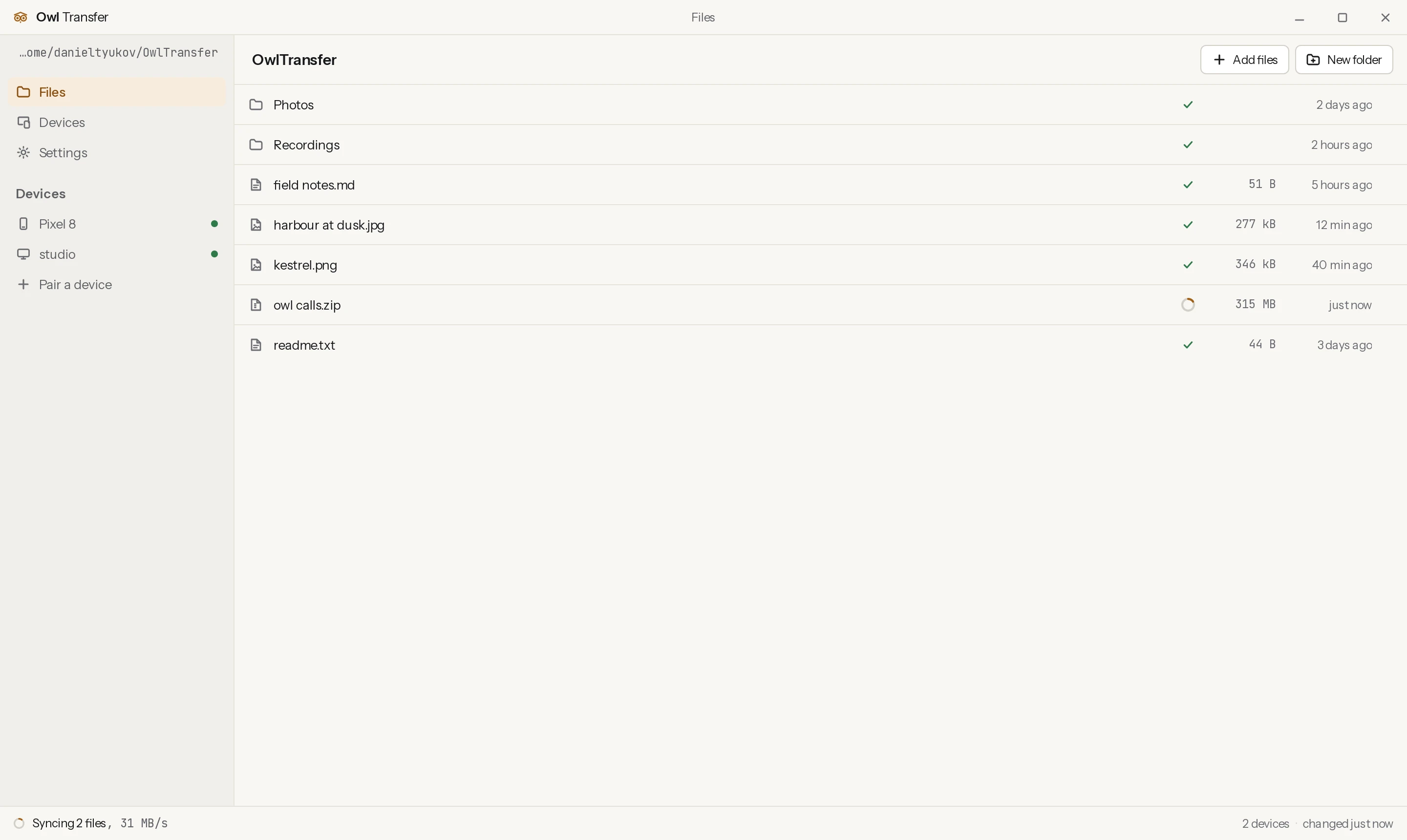 The OwlTransfer desktop app: a sidebar with the sync folder and two paired devices each showing a status dot, a file list in the middle with a sync badge beside every name and one file part way through, and a status strip along the bottom.